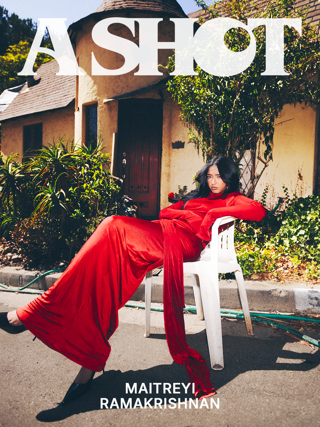 Maitreyi Ramakrishnan in a red dress posed in a plastic chair in the sunlight with text that says 'A Shot' along the top of the image